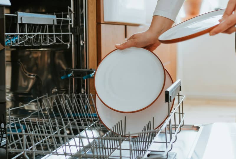 A person taking clean plates from the dishwasher.
