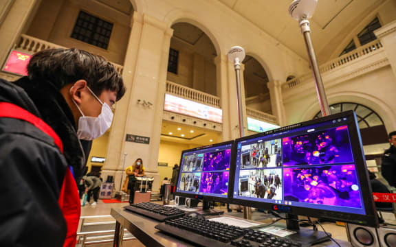 A railway staff member screens arriving passengers with thermal scanners at Hankou station in Wuhan.