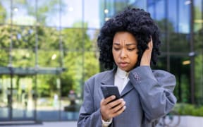 Young woman outside office news reading bad news online, businesswoman using app on smartphone while walking in city, female worker holding phone, sad and disappointed.