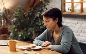 A woman with short dark hair looks down at a sandwich.