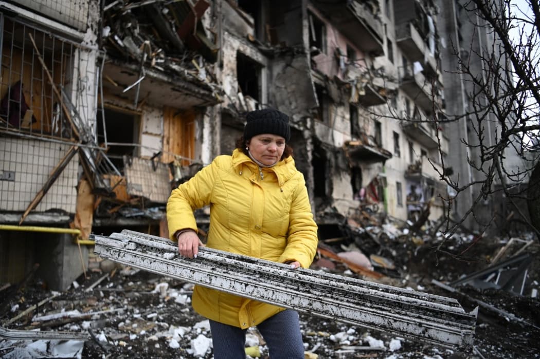 A woman clears debris at a damaged residential building at Koshytsa Street, a suburb of the Ukrainian capital Kyiv, where a military shell allegedly hit, on February 25, 2022.