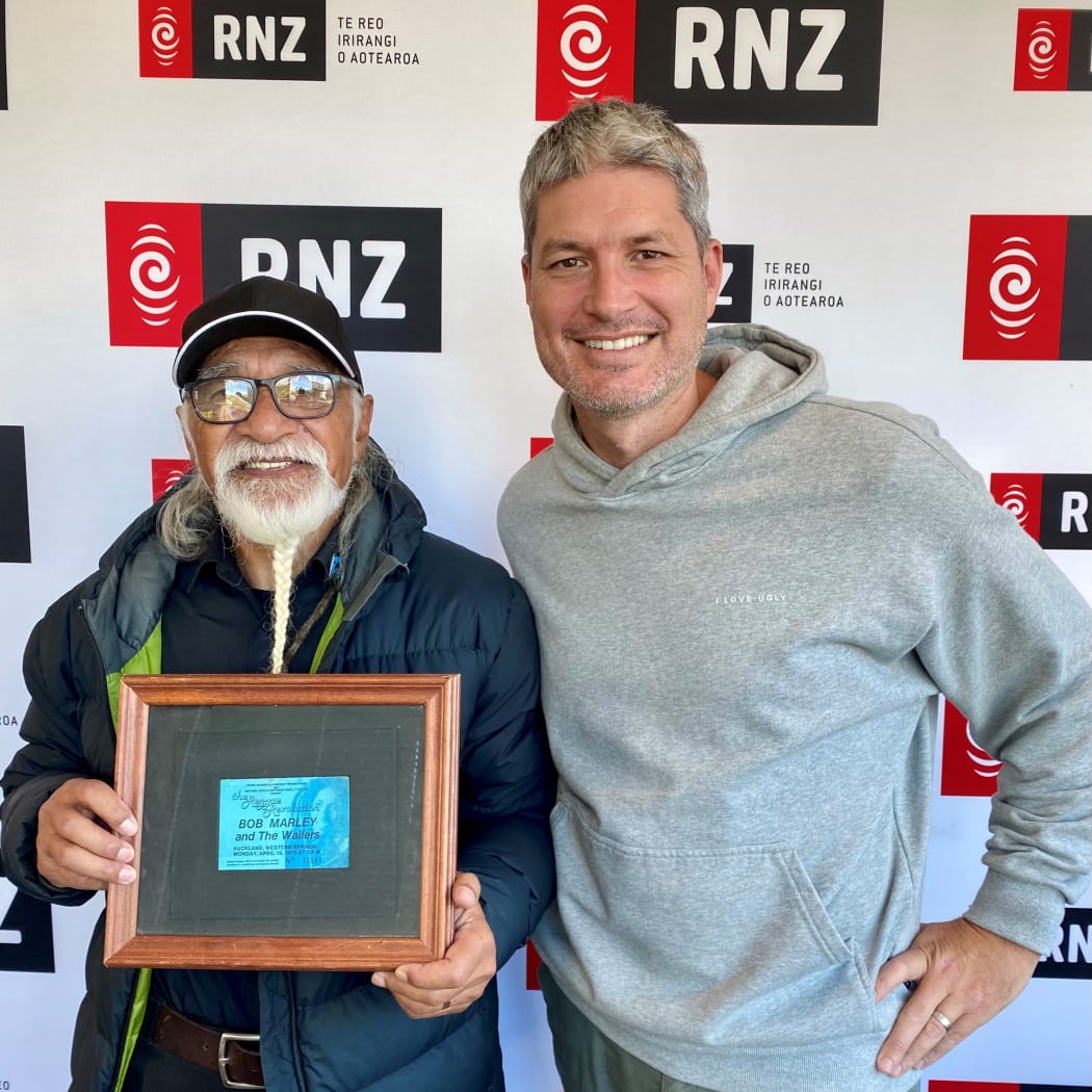 Tigilau Ness and Jesse Mulligan. Tigilau is holding a framed photo of his 1979 ticket to Bob Marley and The Wailers, framed by Te Papa.