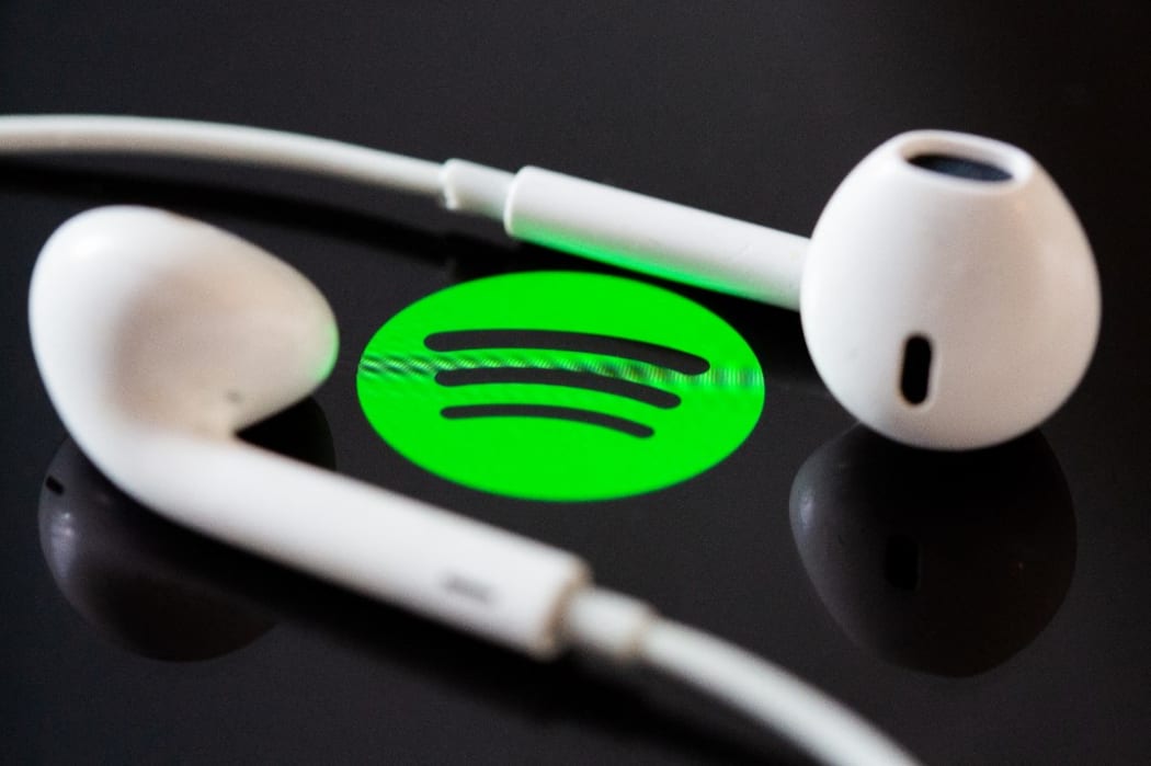 Headphones are on the screen of a smartphone, which displays the logo from the music streaming service Spotify.