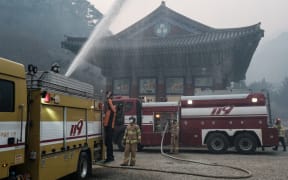 A firefighter controls the water cannon on a fire engine to extinguish the remaining flames after most of the buildings were burned to the ground in a wildfire at Gounsa Temple in Uiseong on March 26, 2025. At least 18 people have been killed in one of South Korea's worst wildfire outbreaks, with multiple blazes burning and causing "unprecedented damage", the acting president said. (Photo by YASUYOSHI CHIBA / AFP)