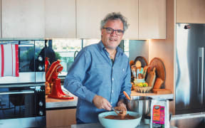 Chef Peter Gordon is whisking a bit bowl of chocolate mousse. Peter is wearing a blue shirt and glasses, and looks towards the camera.