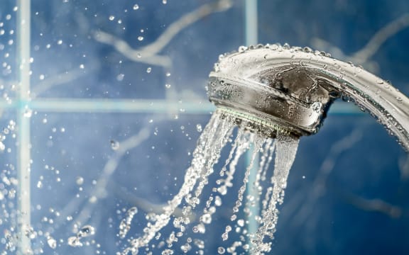 Showerhead with flow of water spilling out on blue background