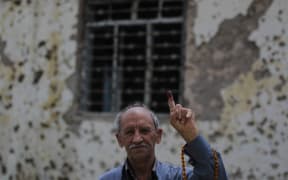 An Iraqi voter shows his ink-stained index finger in front of a damaged wall in western Mosul's Zanjili neighbourhood on May 12, 2018, still partially in ruins from the devastating months-long fight to oust the Islamic State group.
