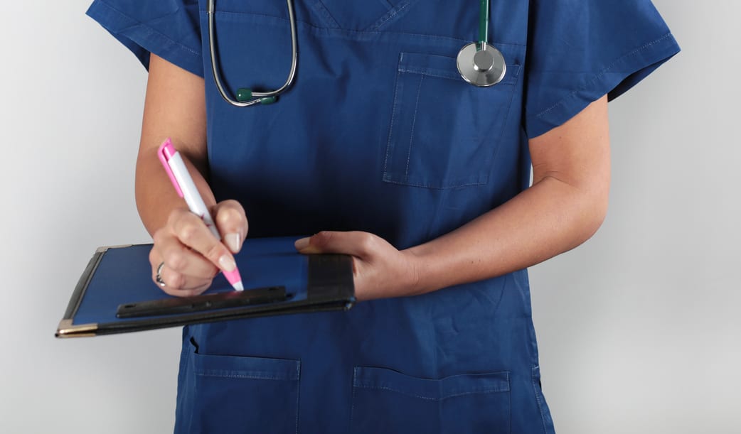 Doctor with a stethoscope writing on a clipboard.