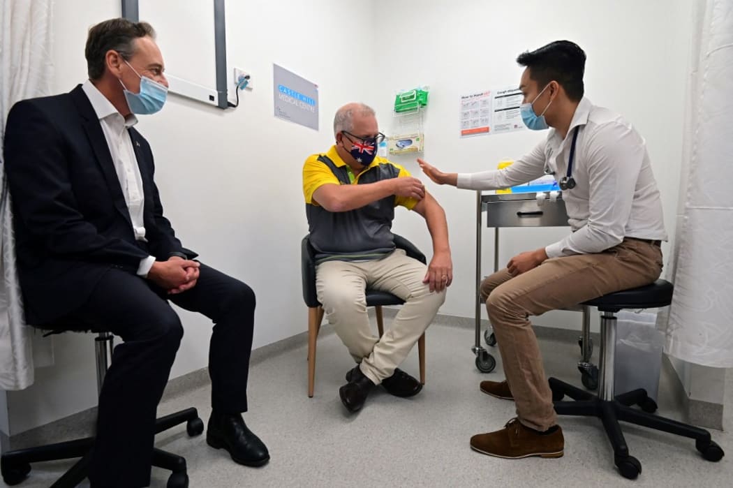 Australia's Prime Minister Scott Morrison (C) rolls up his sleeve before receiving a dose of the Pfizer/BioNTech Covid-19 vaccine, as Minister for Health Greg Hunt (L) looks on, at the Castle Hill Medical Centre in Sydney on February 21, 2021.