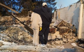 Kyle Kucharski hugs his partner Nicole Perri as they stand on the ruins of their house destroyed by the Palisades Fire in the Pacific Palisades neighborhood of Los Angeles, California on January 10, 2025. When Kyle Kucharski and Nicole Perri moved into their dream home in the Pacific Palisades area of Los Angeles, they bought a crate of wine to mark the realization of a dream, and put it aside for a special day.
That day never came. 
Now after a raging fire destroyed almost the entire neighborhood, all they have left is the empty box with the brand name written across it: Purgatory. (Photo by Cecilia SANCHEZ / AFP)