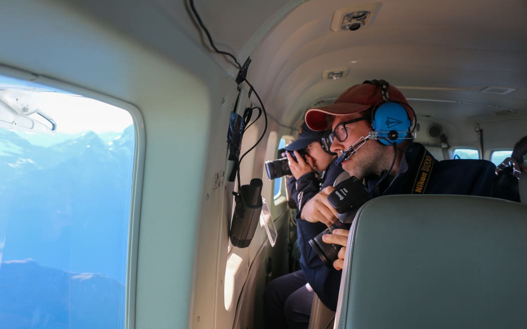 Two people holding cameras look and take photos out of plane windows.