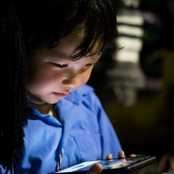 A small boy in a blue shirt gazes down at a phone screen.