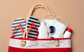 Beach bag with beach items and medical protective mask on beige background. Coronavirus summer concept