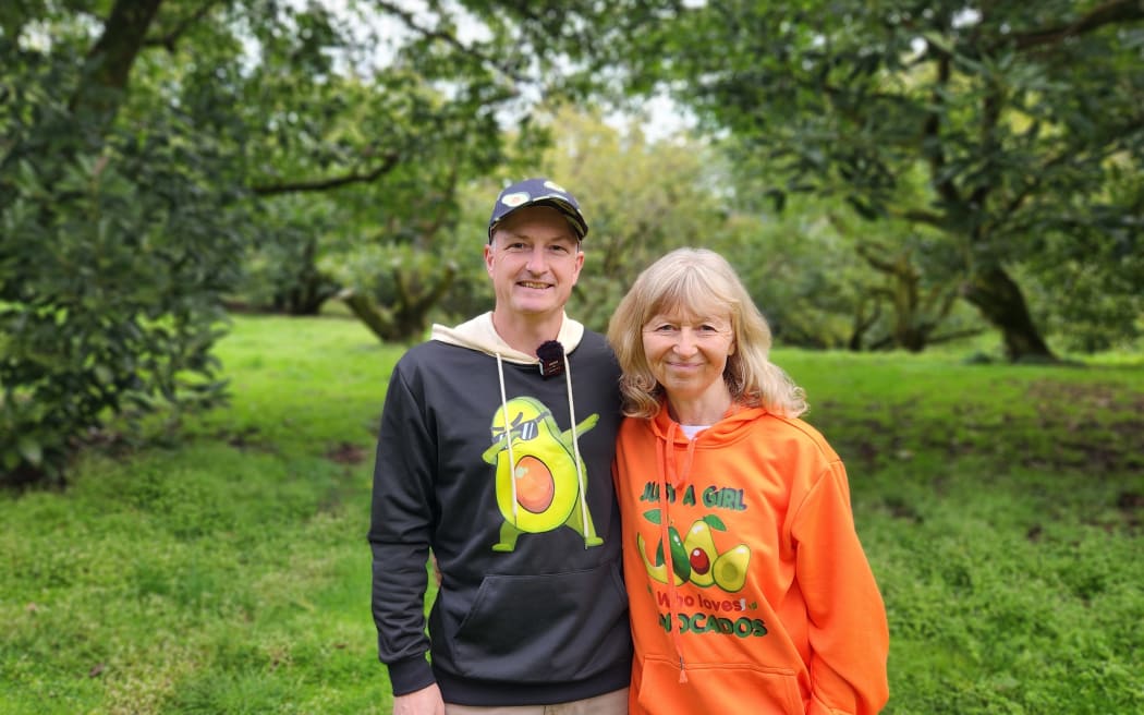 Tim Rosamond and Michele Ricou standing in their orchard, wearing sweatshirts emblazoned with avocados