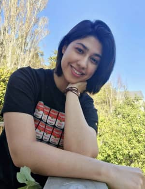 Kiana Jalali - a smiling woman with a dark brown bob - faces the camera with a blue sky and green trees behind her.
