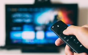 Someone pointing a remote at a television screen which is out of focus in the background.