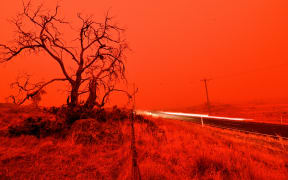 A long exposure picture shows a car commuting on a road as the sky turns red from smoke of the Snowy Valley bushfire on the outskirts of Cooma on January 4, 2020.