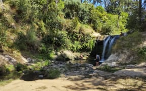 A waterfall with swimmers at the bottom.