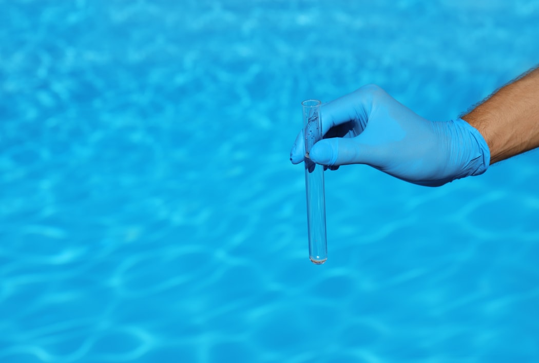 Man holding test tube with water against swimming pool on sunny day.