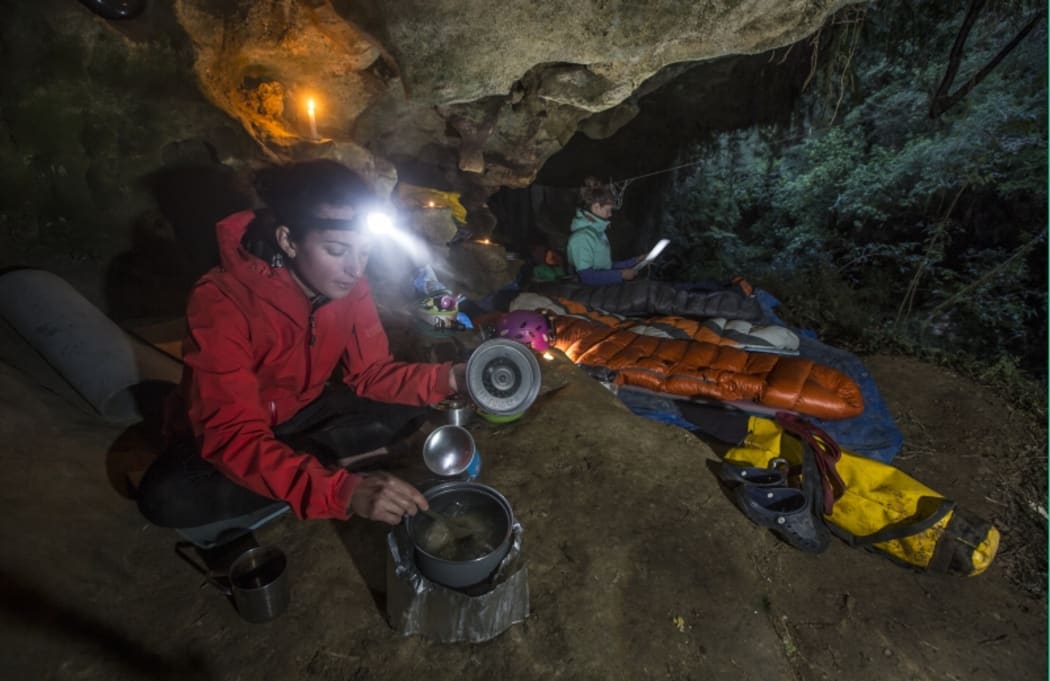 An image showing the cavers preparing dinner at their bivvy underneath a large rock overhang.
