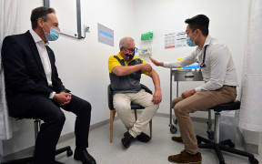 Australia's Prime Minister Scott Morrison (C) rolls up his sleeve before receiving a dose of the Pfizer/BioNTech Covid-19 vaccine, as Minister for Health Greg Hunt (L) looks on, at the Castle Hill Medical Centre in Sydney on February 21, 2021.