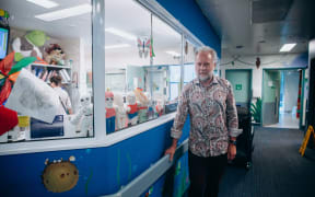 Man in paisely shirt stands new toys in a children's ward