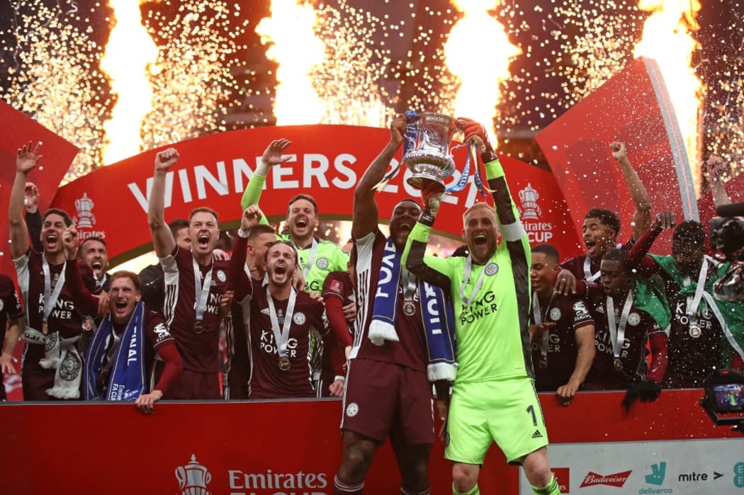 Leicester City's Jamaican defender Wes Morgan (L) and goalkeeper Kasper Schmeichel (R) hold up the winner's trophy as the Leicester players celebrate victory after the English FA Cup final football match  at Wembley Stadium May 15, 2021.