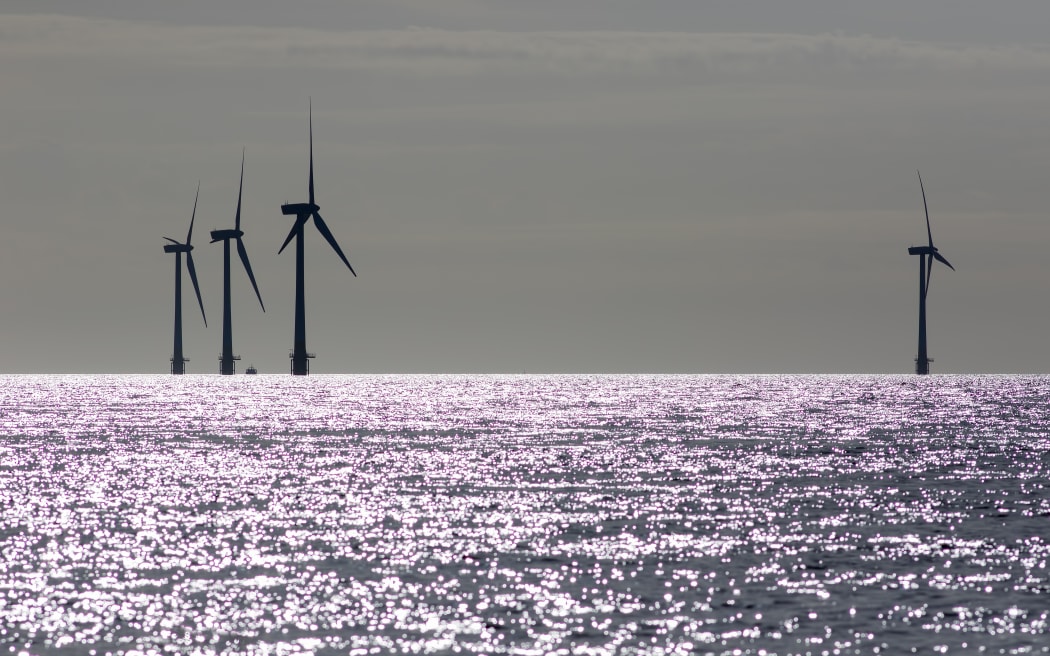 Offshore wind farm wind turbines silhouette. Focus on sea horizon. Picture taken shortly after sunrise. Crisp black sihouetted windmills or turbines in profile. Clean energy production North sea UK.