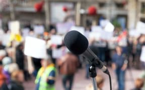 Microphone in focus against blurred protesters.