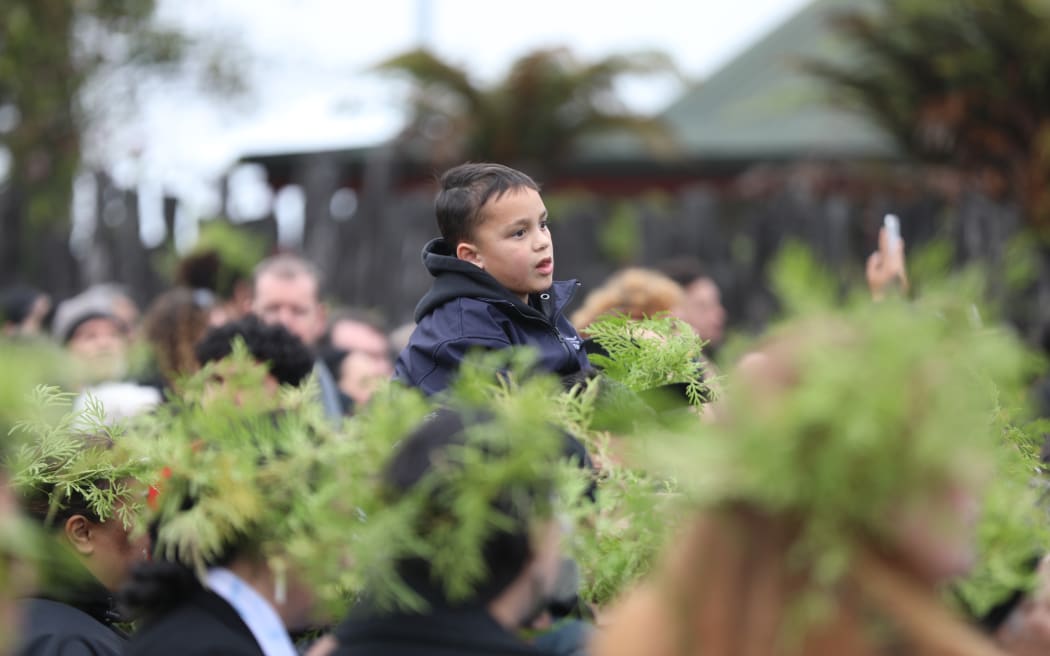 A young boy waits to pay his respects amidst a sea of pare kawakawa at the gates of Tuurangawaewae.