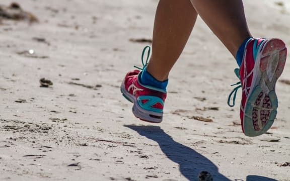 A pair of legs in running shoes move along a beach.