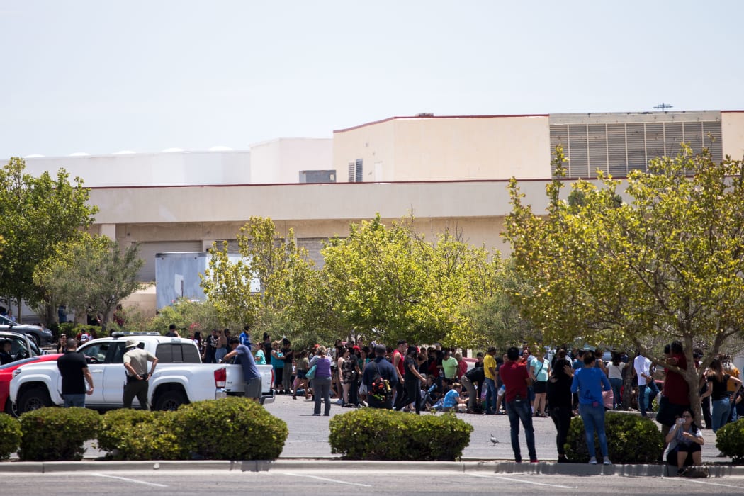 People evacuated from the mall where the shooting took place sit in a parking area.