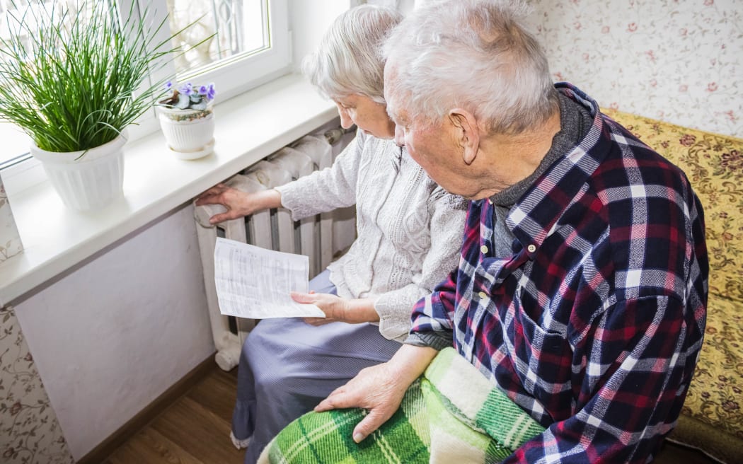 The senior woman holding gas bill in front of heating radiator. Payment for heating in winter.