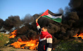 A Palestinian man holds a Palestinian flag during clashes with Israeli forces, near the Israel-Gaza border east of Gaza City, January 26, 2023.