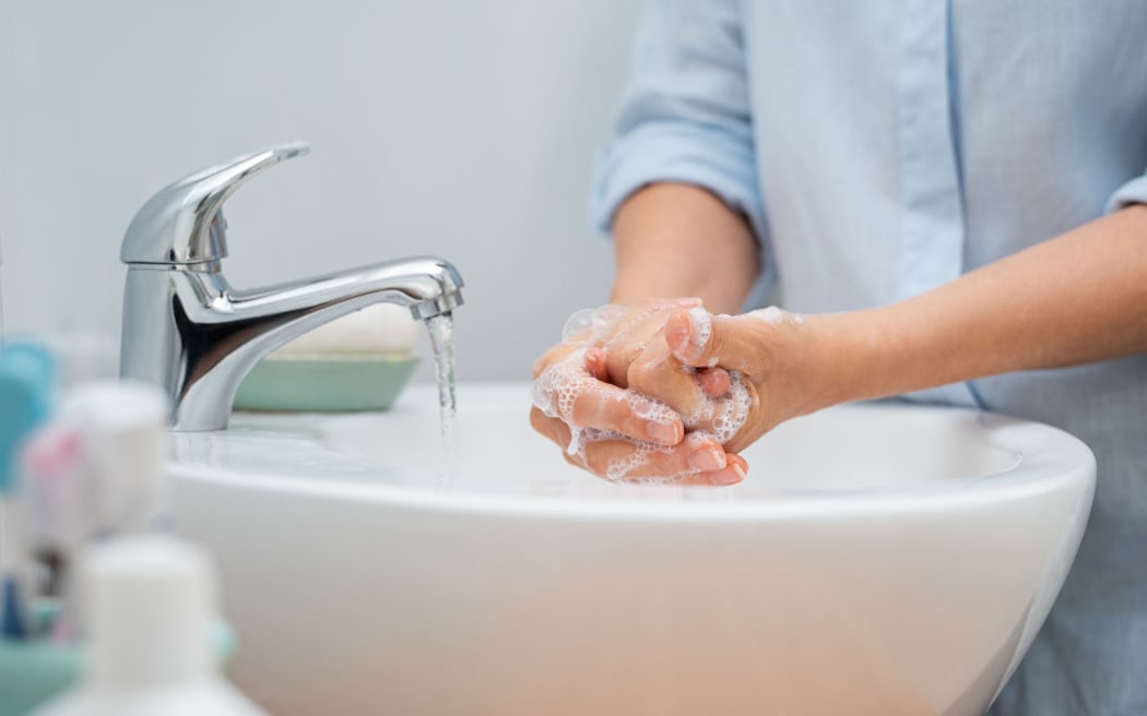 Closeup of woman applying soap while washing hands in basin with open tap. Mature woman washing hands for cleanliness purpose. Lady rubbing hands filled with soap.