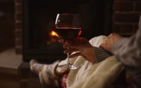 Woman with glass of red wine near burning fireplace, closeup