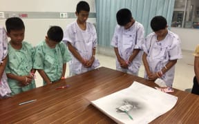 This handout photo released by the Ministry of Health shows members of the rescued "Wild Boars" football team at hospital in Chiang Rai province bowing their heads after writing messages on a drawing of former Navy SEAL diver Saman Kunan who died  during the rescue mission.