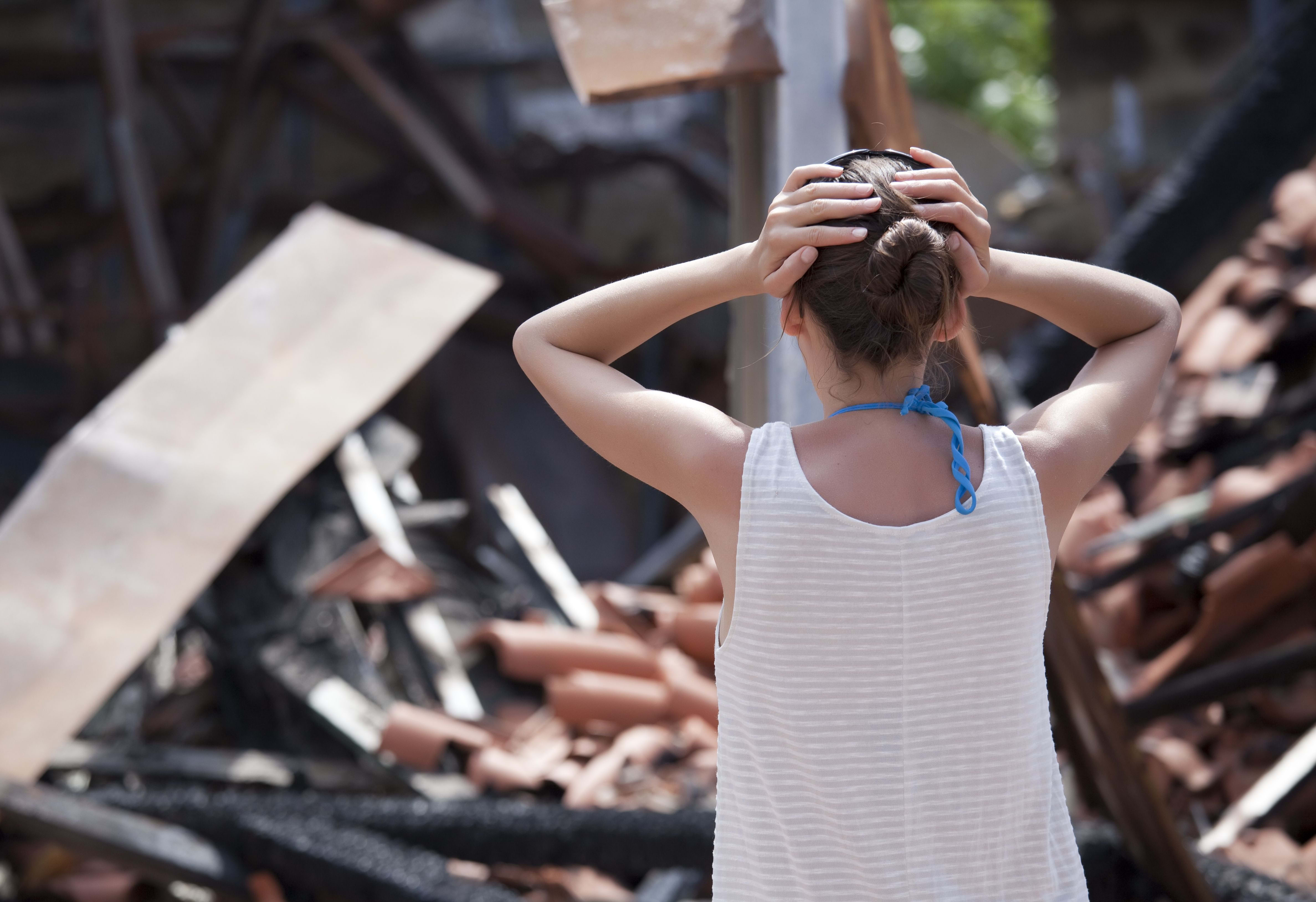 A woman stands with her heads on her hands in front of her burned home.