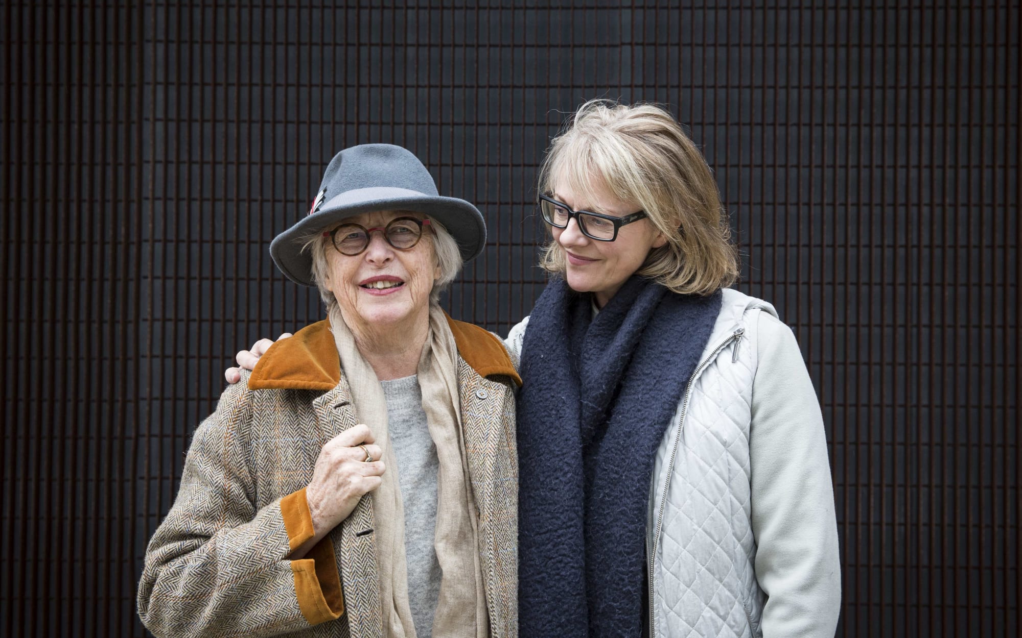 Portrait of the two women standing side by side in front of a dark background