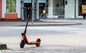 electric scooter or e-scooter parked on sidewalk, blurred city street background - image