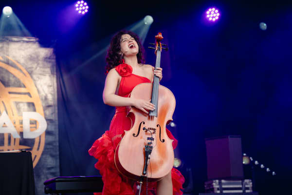 Cuban cellist and singer Ana Carla Maza performing at WOMAD 2025 in New Plymouth. Ana is wearing a red dress and playing a cello while singing.