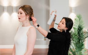 Wellington makeup artist and hair stylist Veronica Zhou in black spraying the hair of someone wearing white for a wedding.