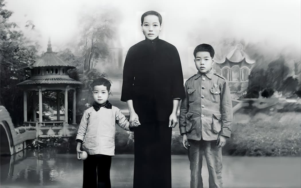 Lack and white photo of Chinese woman in traditional dress holding the hands of two children.