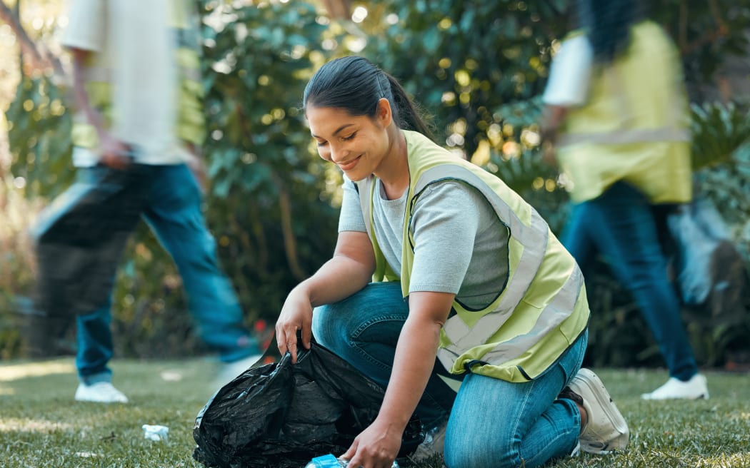 Volunteer helping clean rubbish/trash from park in outdoors grass area.