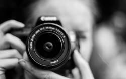 A person holding a camera to their fdace, in black and white.