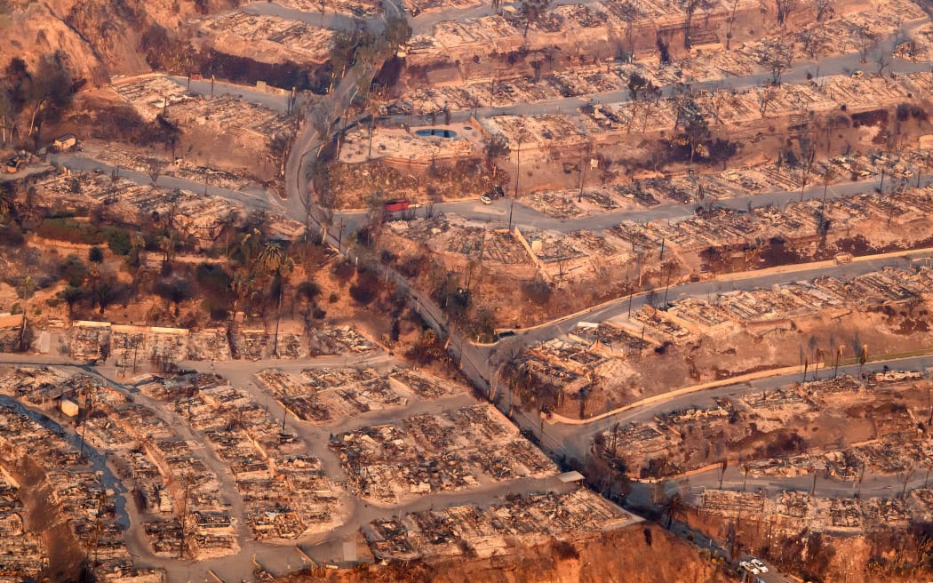 In this aerial view taken from a helicopter, homes burned from the Palisade fire smolder near the Pacific Palisades neighborhood of Los Angeles, California on January 9, 2025. Massive wildfires that engulfed whole neighborhoods and displaced thousands in Los Angeles remained totally uncontained January 9, 2025, authorities said, as US National Guard soldiers readied to hit the streets to help quell disorder. Swaths of the United States' second-largest city lay in ruins, with smoke blanketing the sky and an acrid smell pervading almost every building. (Photo by JOSH EDELSON / AFP)