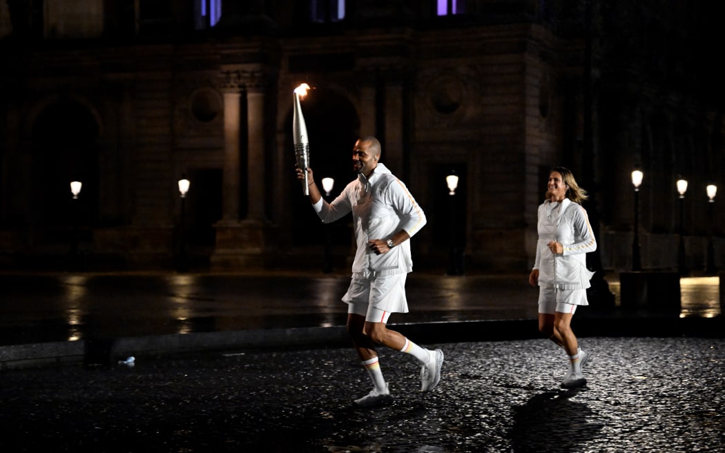 Torchbearer French former basketball player Tony Parker holds the Olympic flame next to French former tennis player Amelie Mauresmo during the opening ceremony of the Paris 2024 Olympic Games in Paris on July 26, 2024, as the Louvre Museum is seen in the background. (Photo by Olivier MORIN / AFP)