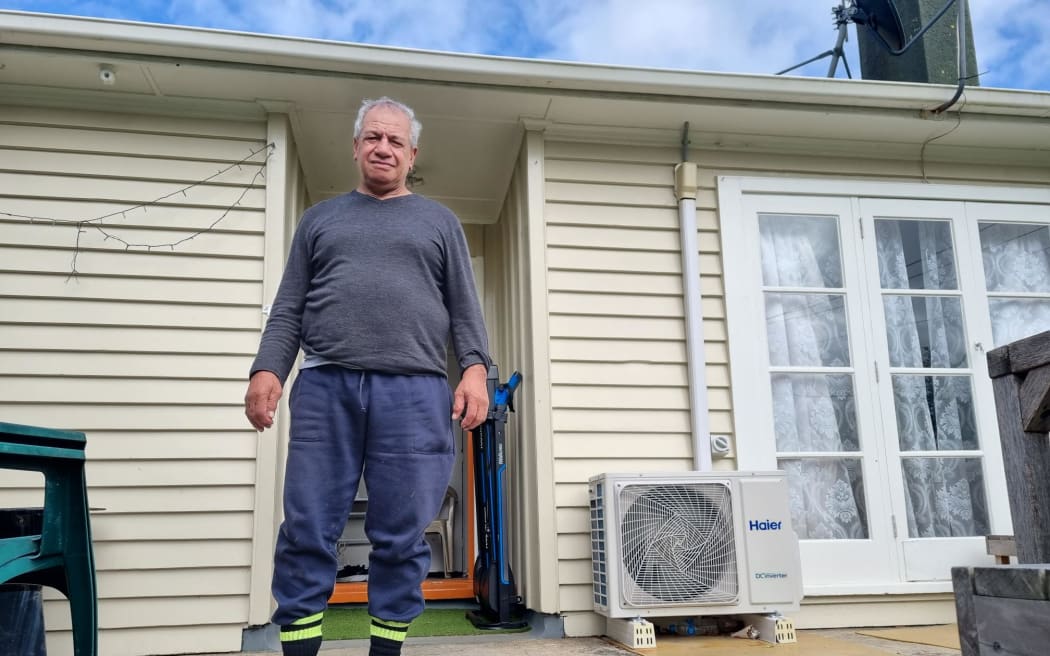 Steven Schaunkel stands in front of his house wearing a grey long sleeve top, blue pants and black and bright yellow socks.