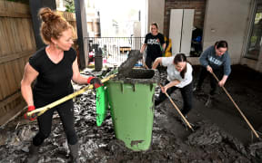People clear mud from a property damaged by floods in the Melbourne suburb of Maribyrnong on October 15, 2022. - Australia reported the first fatality from days of widespread flash flooding on October 15, 2022 despite heavy rains easing and flood levels topping out across much of the southeast. Hundreds of homeowners began a long clean-up after storm waters engulfed streets, houses and cars across three states, with Melbourne suburbs among the worst hit. (Photo by William WEST / AFP)