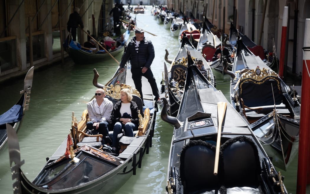 A gondolier sails with two customers near San Marco Square in Venice, on April 25, 2024. The new strategy to lower the number of tourists visiting the UNESCO World Heritage site calls for day-trippers to pay a five-euro ticket to enter the historic city centre and is due to start on April 25. (Photo by MARCO BERTORELLO / AFP)